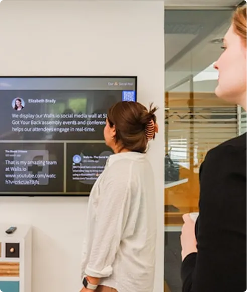 Two women looking at a digital display screen in an office.